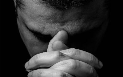 Photo of a man's face with his hands clasped in front of him in prayer, to illustrate the article Why Pray?